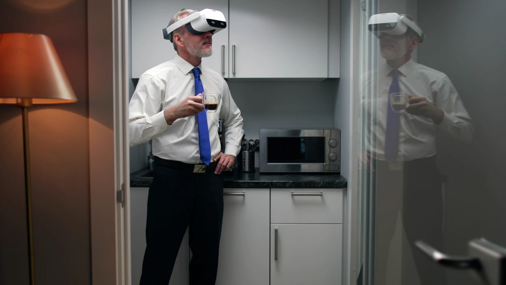Muž má na sebe okuliare na virtuálnu realitu a pritom pije kávu v kuchyni